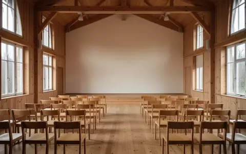Ein leerer, sonnendurchfluteter Gemeinschaftssaal mit hölzernen Stuhlreihen in einer ruhigen, minimalistischen Umgebung. - Foto: über boerse-global.de