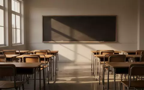 Ein leerer, sonnendurchfluteter Klassenraum mit leeren Holztischen und Stühlen vor einer leeren Schultafel. - Foto: über boerse-global.de