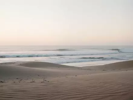 Ein ruhiger, minimalistischer Küstenabschnitt am frühen Morgen mit sanften Sanddünen und auslaufenden Wellen, die eine friedliche Atmosphäre ausstrahlen. - Foto: über boerse-global.de