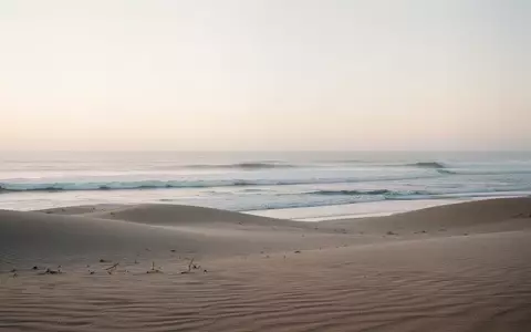 Ein ruhiger, minimalistischer Küstenabschnitt am frühen Morgen mit sanften Sanddünen und auslaufenden Wellen, die eine friedliche Atmosphäre ausstrahlen. - Foto: über boerse-global.de