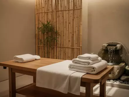 Ein ruhiger, minimalistischer Behandlungsraum mit einer leeren Massageliege, weißen Handtüchern und einem kleinen Brunnen. - Foto: über boerse-global.de