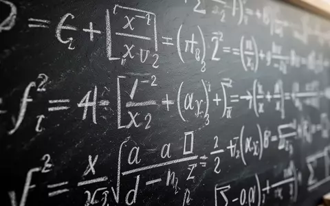 Nahaufnahme komplexer mathematischer Gleichungen, die mit weißer Kreide auf eine dunkle Schiefertafel geschrieben wurden. - Foto: über boerse-global.de