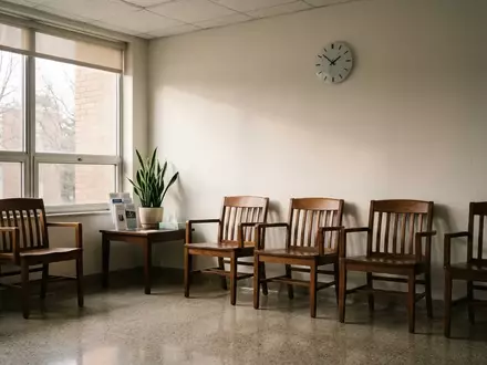 Ein leerer, minimalistischer Wartebereich in einer medizinischen Einrichtung mit schlichten Holzstühlen und Tageslicht. - Foto: über boerse-global.de