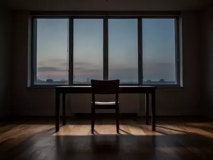 Ein minimalistischer, ruhiger Arbeitsraum mit leerem Stuhl vor einem Fenster in der Abenddämmerung. - Foto: über boerse-global.de