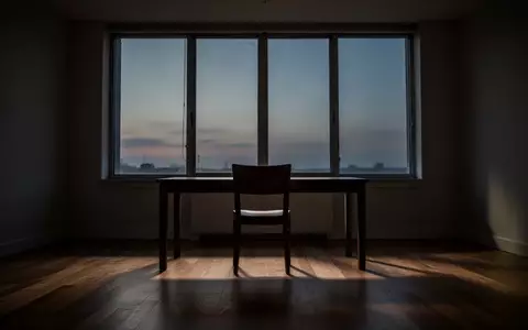 Ein minimalistischer, ruhiger Arbeitsraum mit leerem Stuhl vor einem Fenster in der Abenddämmerung. - Foto: über boerse-global.de