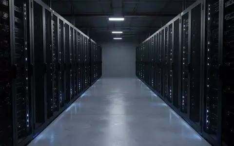 Dunkler, industrieller Serverraum mit leeren, unbeleuchteten Server-Racks und blauem Umgebungslicht auf einem Betonboden. - Foto: über boerse-global.de