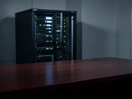 Ein dunkler, modern eingerichteter Raum mit einem Server-Rack im unscharfen Hintergrund und einer leeren Schreibtischfläche. - Foto: über boerse-global.de