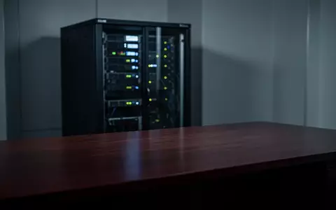 Ein dunkler, modern eingerichteter Raum mit einem Server-Rack im unscharfen Hintergrund und einer leeren Schreibtischfläche. - Foto: über boerse-global.de