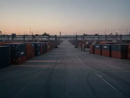 Ein weitläufiges Logistikterminal mit ordentlich gestapelten Containern in der Abenddämmerung. - Foto: über boerse-global.de