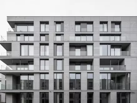 Moderne, minimalistische Fassade eines Wohngebäudes aus Stein und Glas bei bewölktem Himmel. - Foto: über boerse-global.de
