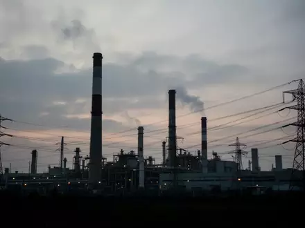 Die Silhouette einer industriellen Fabrikanlage vor einem bewölkten Dämmerungshimmel bei ruhigem Licht. - Foto: über boerse-global.de
