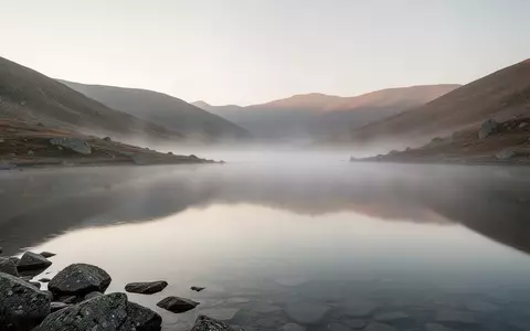 Ein ruhiger, nebliger Bergsee bei Tagesanbruch als Symbol für Stille und Entschleunigung. - Foto: über boerse-global.de