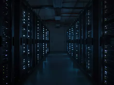 Dunkler Serverraum mit blau leuchtenden Statusanzeigen an Hardware-Racks. - Foto: über boerse-global.de