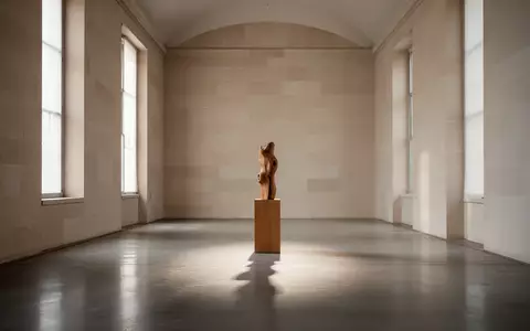 Ein minimalistischer, lichtdurchfluteter Ausstellungsraum mit einer einzelnen Holzskulptur und langen Schatten auf dem Boden. - Foto: über boerse-global.de