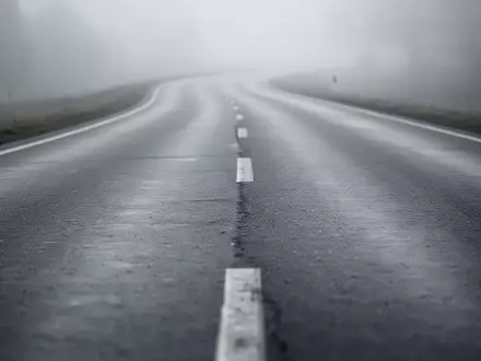 Eine neblige, leere Landstraße aus Asphalt führt in die Ferne, Fokus auf die Textur des Straßenbelags. - Foto: über boerse-global.de
