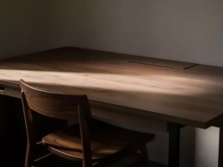 Ein leerer, modern eingerichteter Arbeitsplatz mit einem Holztisch und einem Stuhl bei gedimmtem Licht. - Foto: über boerse-global.de
