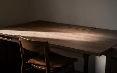 Ein leerer, modern eingerichteter Arbeitsplatz mit einem Holztisch und einem Stuhl bei gedimmtem Licht. - Foto: über boerse-global.de