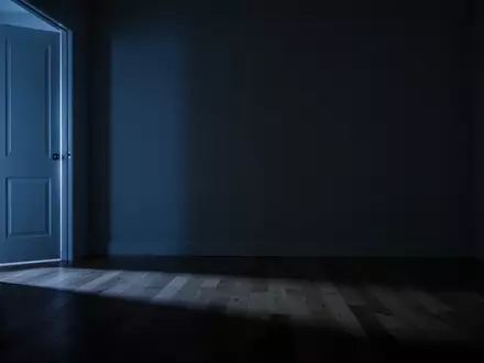 Ein schlafzimmerähnlicher Raum bei Nacht, der nur von einem schwachen Lichtschein unter einer Tür beleuchtet wird. - Foto: über boerse-global.de