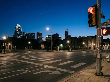 Eine leere Straßenkreuzung in Austin bei Dämmerung mit einer Ampelanlage vor einer verschwommenen Skyline. - Foto: über boerse-global.de