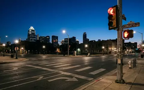 Eine leere Straßenkreuzung in Austin bei Dämmerung mit einer Ampelanlage vor einer verschwommenen Skyline. - Foto: über boerse-global.de