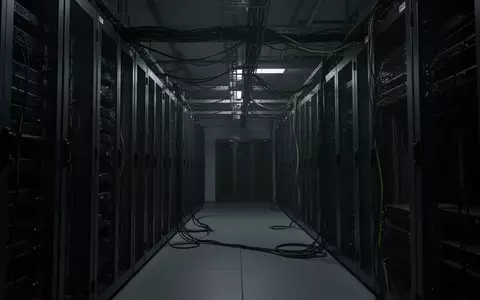 Dunkler, industrieller Serverraum mit leeren Serverschränken und komplexer Verkabelung in einer minimalistischen Umgebung. - Foto: über boerse-global.de
