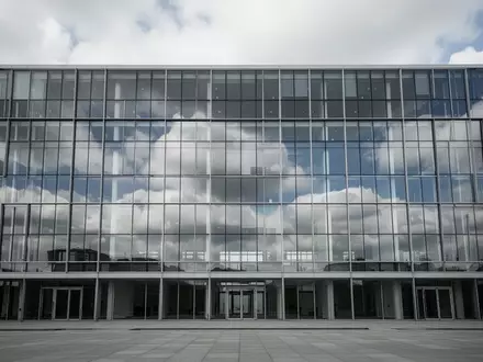 Ein modernes, leeres Bürogebäude mit Glasfassade spiegelt den bewölkten Himmel wider. - Foto: über boerse-global.de