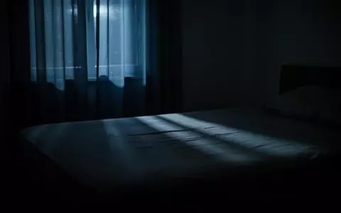 Ein dunkles Schlafzimmer bei Nacht, in das durch einen Vorhang ein schwacher, bläulicher Lichtschein fällt. - Foto: über boerse-global.de