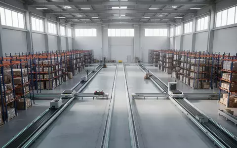 Eine moderne, weitläufige Industriehalle mit leeren Transportwegen und Regalsystemen in einer geordneten, hellen Umgebung. - Foto: über boerse-global.de