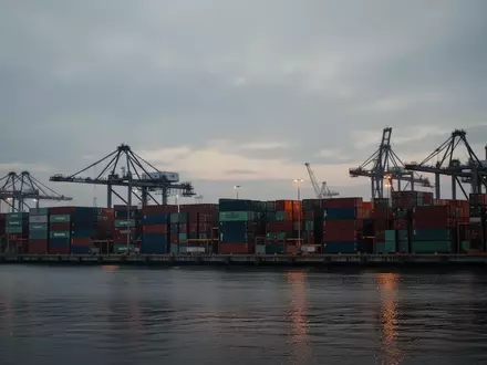 Blick auf einen industriellen Containerhafen mit Kränen und gestapelten Frachtcontainern bei Dämmerung. - Foto: über boerse-global.de