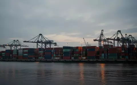Blick auf einen industriellen Containerhafen mit Kränen und gestapelten Frachtcontainern bei Dämmerung. - Foto: über boerse-global.de