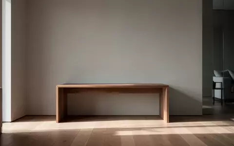 Ein minimalistisch eingerichteter Wohnraum mit einem leeren Holztisch vor einer grauen Wand bei natürlichem Lichteinfall. - Foto: über boerse-global.de