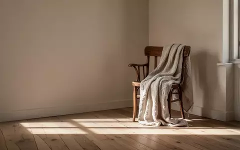 Ein minimalistisch eingerichteter Wohnraum mit einem einzelnen Holzstuhl und einer Decke in einem hellen, lichtdurchfluteten Zimmer. - Foto: über boerse-global.de