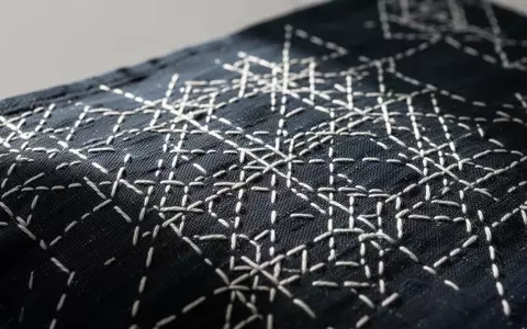 Nahaufnahme einer dunkelblauen Baumwolltextilie mit feinen weißen geometrischen Stickmustern in Sashiko-Technik. - Foto: über boerse-global.de
