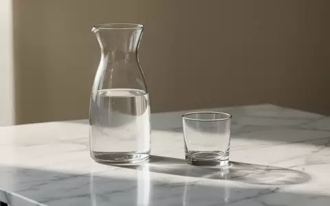 Ein Glas Wasser und eine Glaskaraffe auf einer weißen Marmoroberfläche bei hellem Tageslicht. - Foto: über boerse-global.de