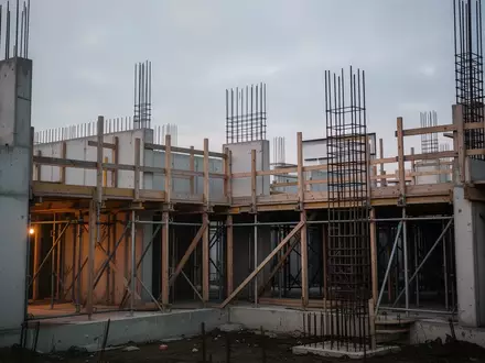 Halb fertiggestellter Rohbau eines Wohngebäudes bei Dämmerung mit Betonwänden und Gerüst. - Foto: über boerse-global.de
