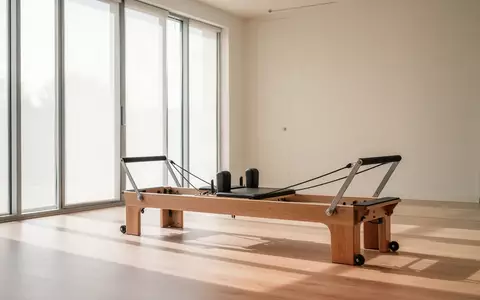 Ein heller, minimalistischer Pilates-Raum mit einem hölzernen Reformer-Gerät vor großen Fenstern bei natürlichem Tageslicht. - Foto: über boerse-global.de