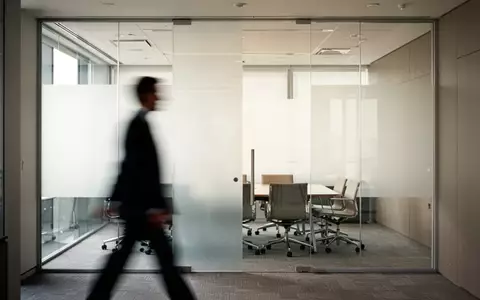 Ein moderner, minimalistischer Büroraum mit einer verschwommenen Silhouette einer Führungskraft im Hintergrund. - Foto: über boerse-global.de