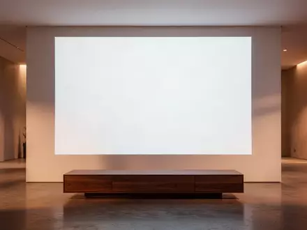 Ein minimalistisch gestaltetes, modernes Wohnzimmer bei Dämmerung mit einer leeren, weißen Projektionsfläche an der Wand. - Foto: über boerse-global.de