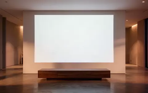 Ein minimalistisch gestaltetes, modernes Wohnzimmer bei Dämmerung mit einer leeren, weißen Projektionsfläche an der Wand. - Foto: über boerse-global.de