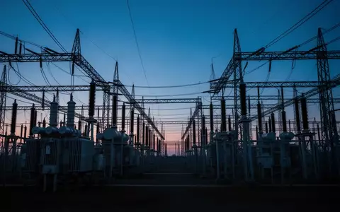 Ein großes, industrielles Umspannwerk bei Dämmerung, das die physische Infrastruktur eines Stromnetzes darstellt. - Foto: über boerse-global.de
