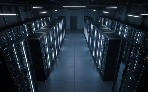 Ein dunkler, symmetrischer Serverraum mit blau beleuchteten Server-Racks in einer minimalistischen, industriellen Umgebung. - Foto: über boerse-global.de