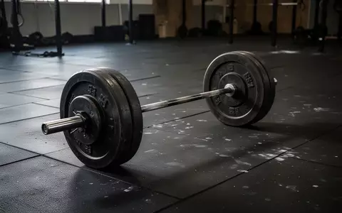 Eine schwere Eisenhantel liegt einsam auf dem Boden eines dunklen, leeren Fitnessstudios. - Foto: über boerse-global.de