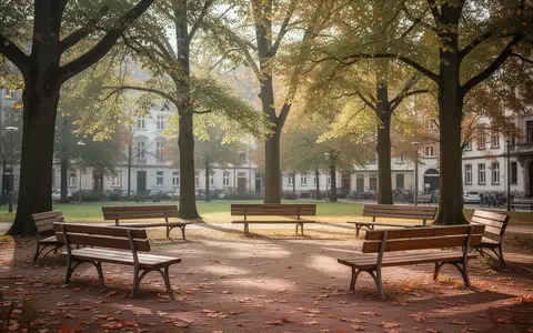 Ein sonniger, einladender Stadtpark mit leeren Holzbänken unter Bäumen im Herbst, der eine ruhige Gemeinschaftsatmosphäre vermittelt. - Foto: über boerse-global.de