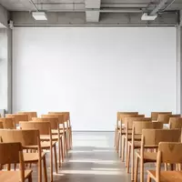 Ein minimalistischer, heller Seminarraum mit leeren Stühlen vor einer neutralen weißen Wand. - Foto: über boerse-global.de