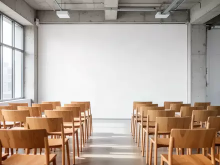 Ein minimalistischer, heller Seminarraum mit leeren Stühlen vor einer neutralen weißen Wand. - Foto: über boerse-global.de