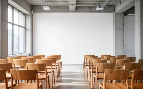 Ein minimalistischer, heller Seminarraum mit leeren Stühlen vor einer neutralen weißen Wand. - Foto: über boerse-global.de