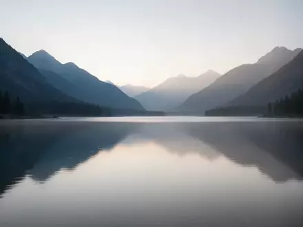 Eine ruhige Berglandschaft mit einem stillen See im sanften Licht der Morgendämmerung, die eine meditative Atmosphäre ausstrahlt. - Foto: über boerse-global.de
