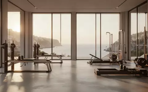Ein minimalistisches, lichtdurchflutetes Fitnessstudio mit hochwertigen Trainingsgeräten und Blick auf eine Küstenlandschaft. - Foto: über boerse-global.de
