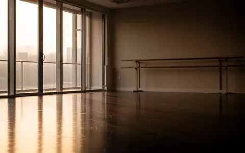 Ein leeres Ballettstudio mit poliertem Holzboden und einer Ballettstange vor einer schlichten Wand bei ruhigem Tageslicht. - Foto: über boerse-global.de
