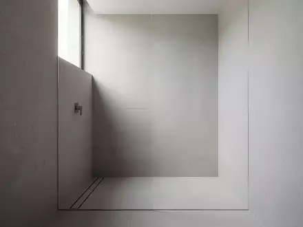 Minimalistisches Badezimmer mit nahtlosen grauen Steinoberflächen, ebenerdiger Dusche und architektonischer Klarheit. - Foto: über boerse-global.de